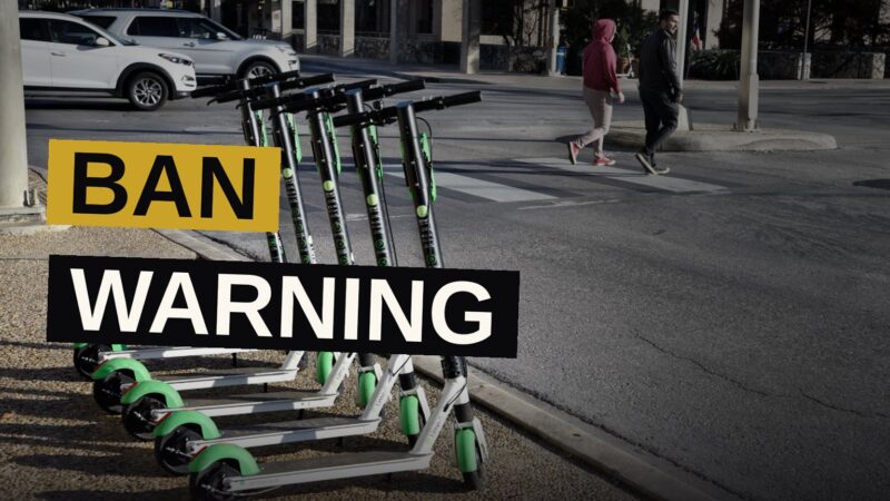 Students riding electric scooters and e-bikes navigate a crowded walkway on a college campus.