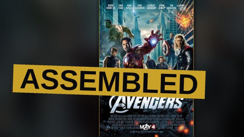 The Avengers team stands together on a New York street, with the Hulk roaring and Iron Man flying overhead amid alien ships.