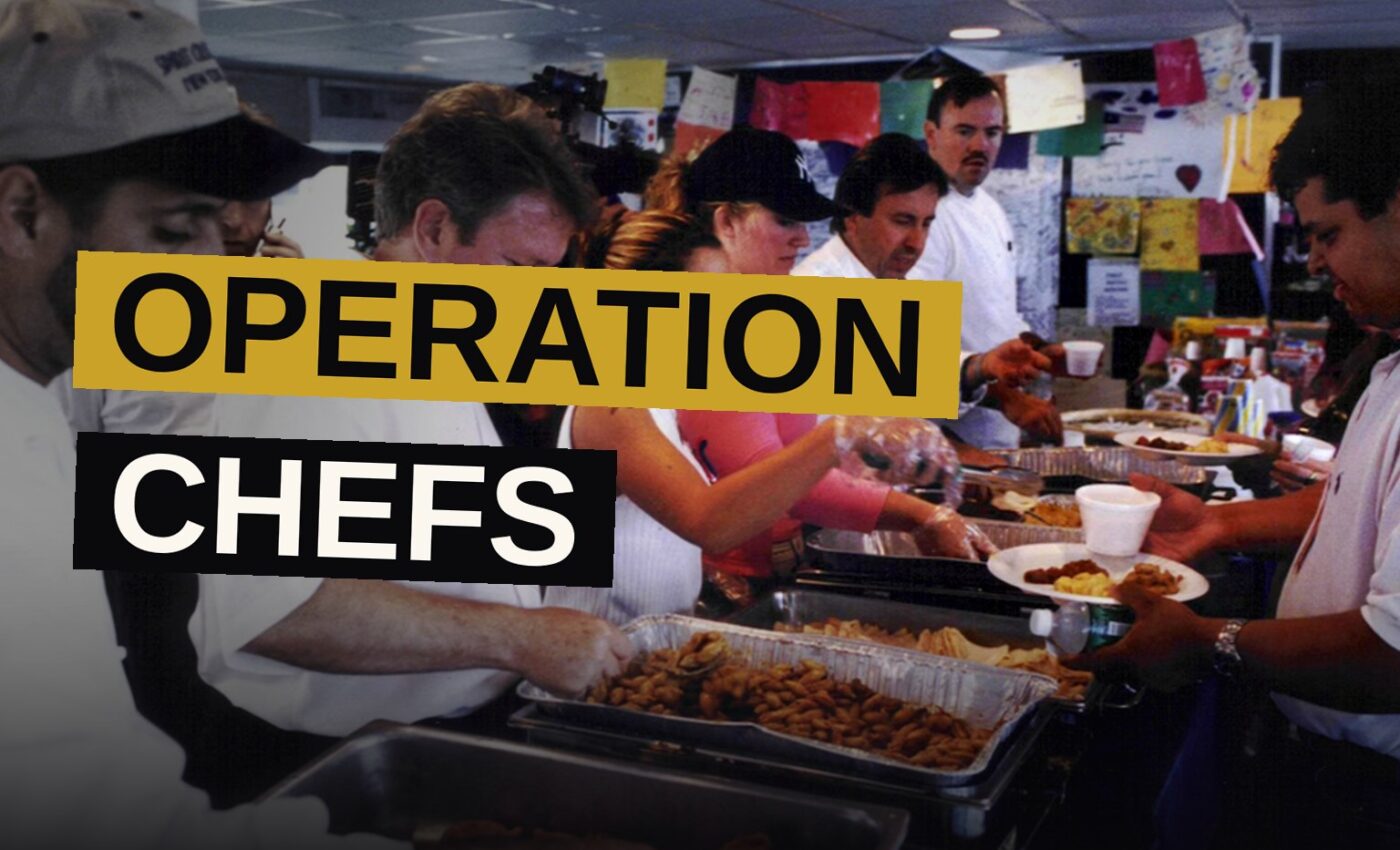 Chefs prepare meals on a barge kitchen with the Manhattan skyline behind them.