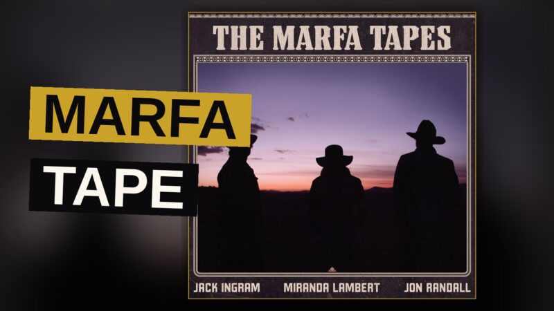 Three musicians sit beneath a desert sky, their instruments resting beside them as the sun sets.