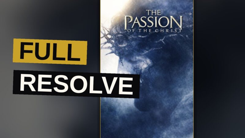 A robed man kneels in a dim stone corridor, his face marked with sorrow and suffering.