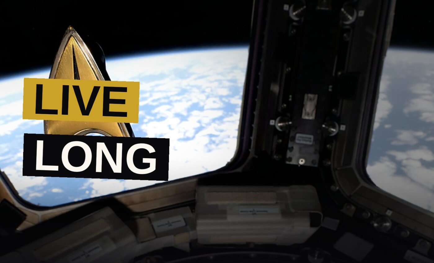 An astronaut on the station shows a hand sign while wearing a small badge, with Earth glowing beyond the window.