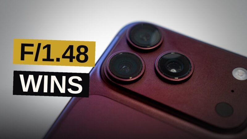 Close-up of an iPhone 18 Pro camera housing with a metallic iris ring and glass lens on a dark surface.