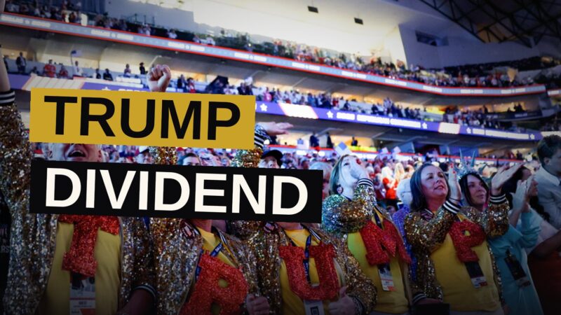 A political rally in a large arena with a speaker on stage and many empty seats.