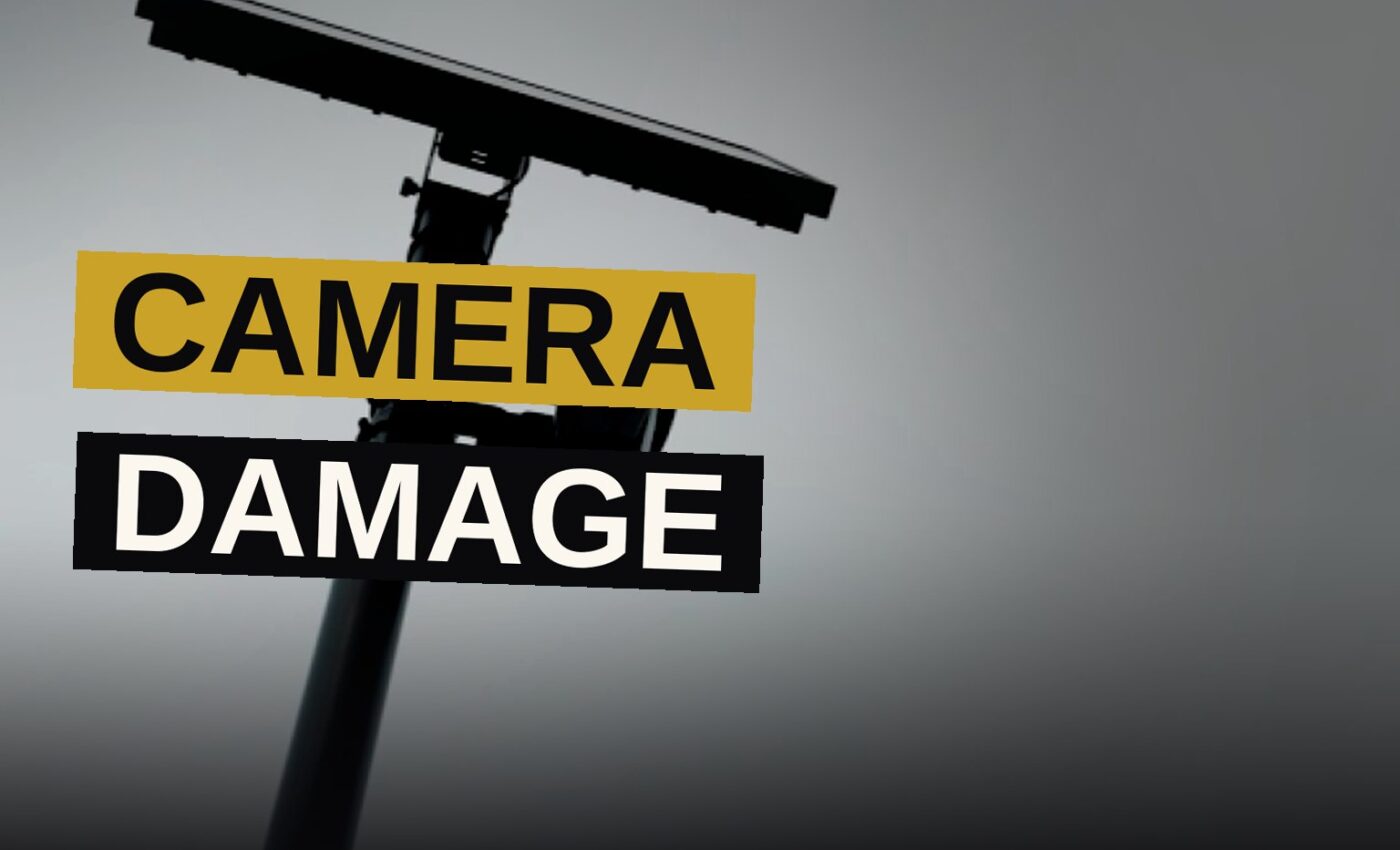 A damaged security camera rests on the ground beside a city street.