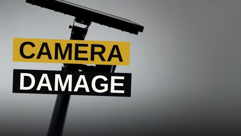 A damaged security camera rests on the ground beside a city street.