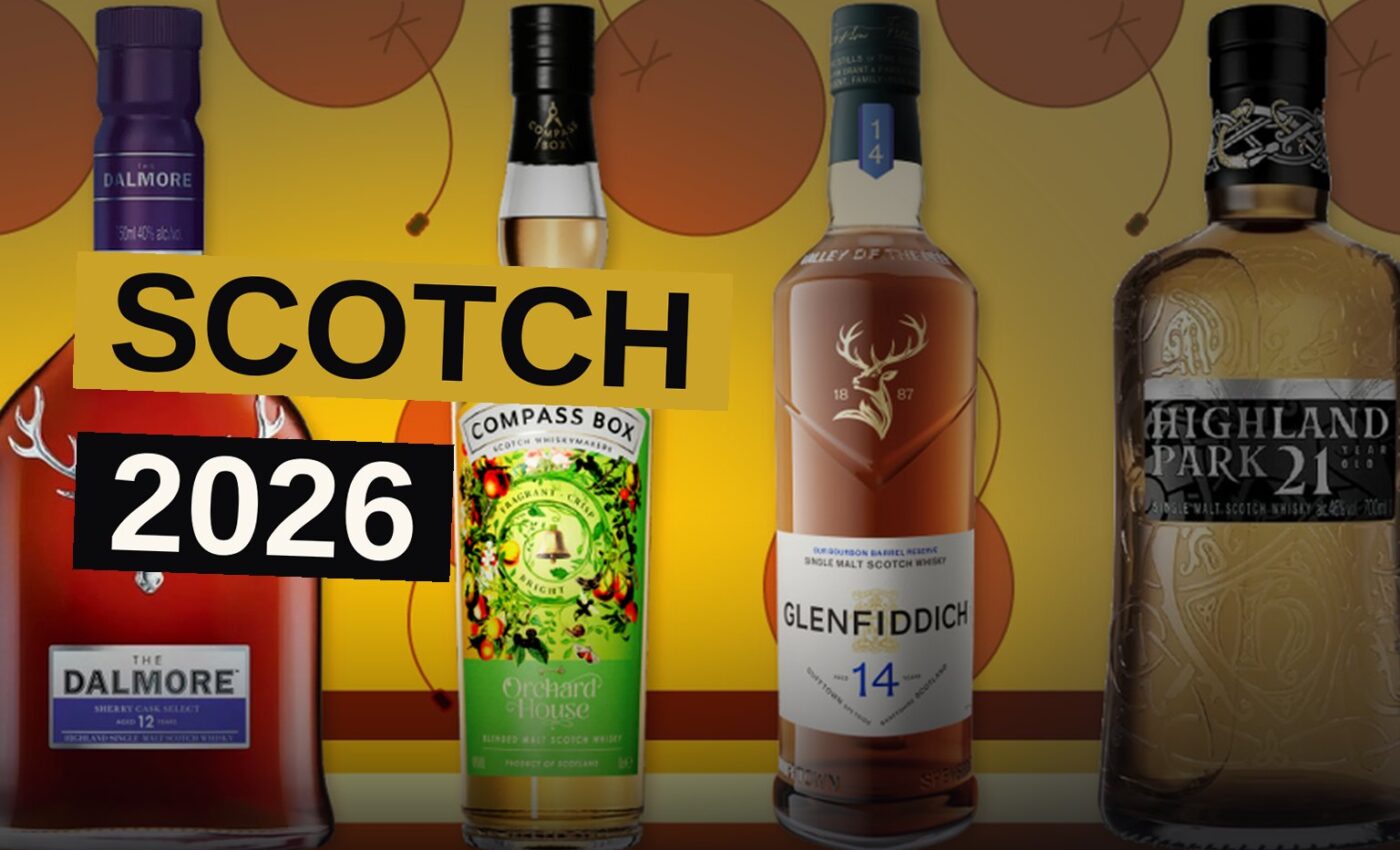 A Glencairn glass of Scotch whisky sits on a wooden bar, with blurred bottles and warm lighting in the background.