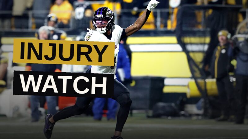 A Baltimore Ravens wide receiver in a purple jersey runs a drill on a sunny practice field.